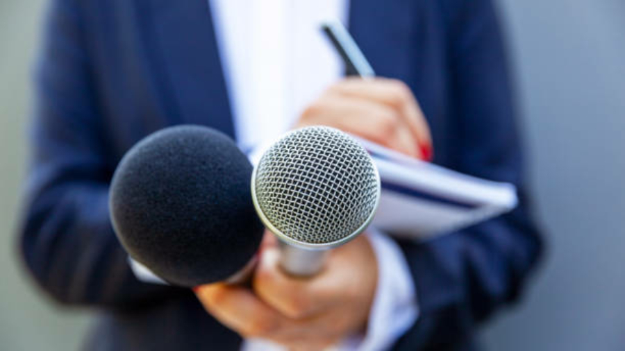 News reporter or TV journalist at press conference, holding microphone and writing notes