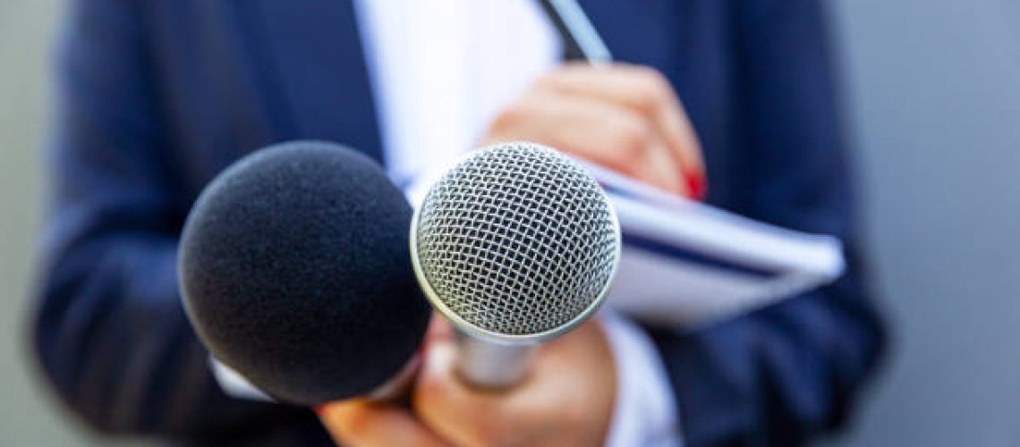 News reporter or TV journalist at press conference, holding microphone and writing notes